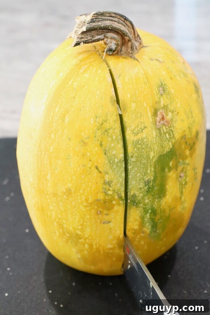 A spaghetti squash being carefully sliced down the middle on a wooden cutting board with a large knife.