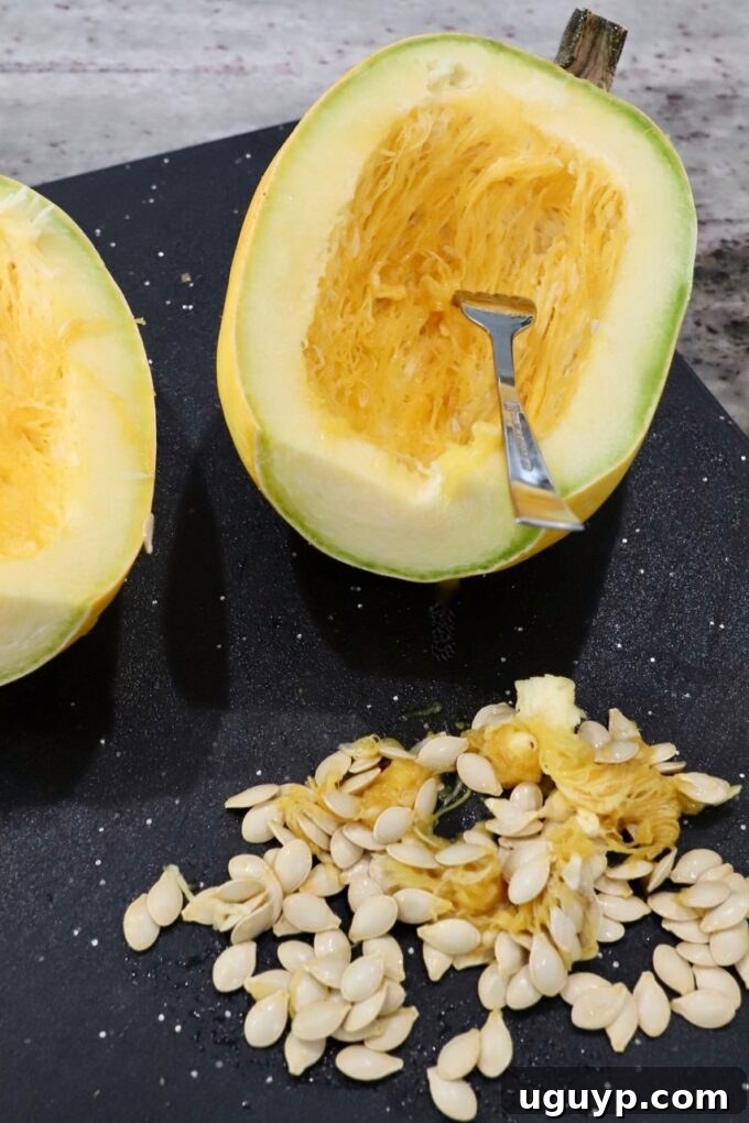 A spaghetti squash halved on a cutting board, with seeds and pulp removed and placed to the side.