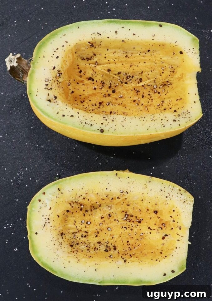 Two halves of spaghetti squash seasoned with olive oil, salt, and pepper on a cutting board.