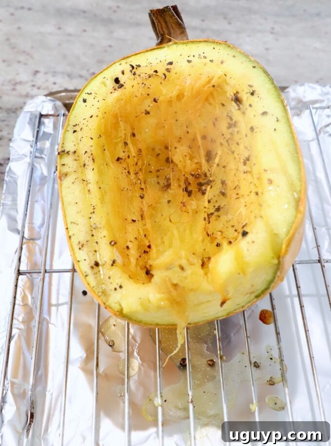 A roasted spaghetti squash half on a wire rack, still on the baking sheet, with a fork starting to pull out strands.