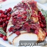 Sliced cranberry glazed turkey breast on a white plate with fresh thyme sprigs