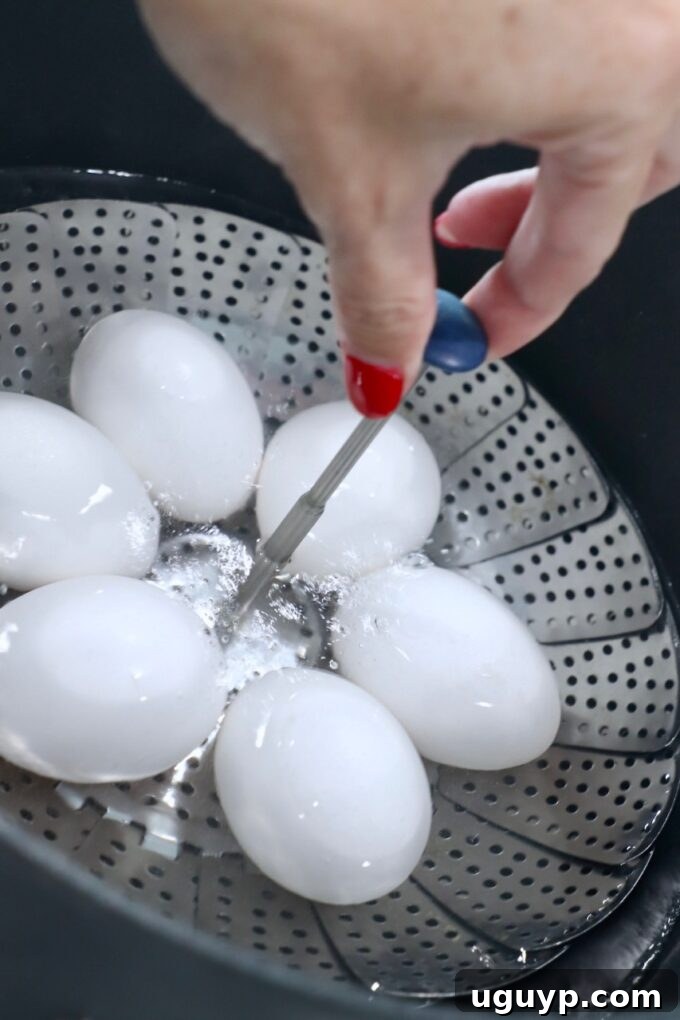 A hand gently lowering eggs in a metal steamer basket into a large pot of vigorously boiling water on a stove top.