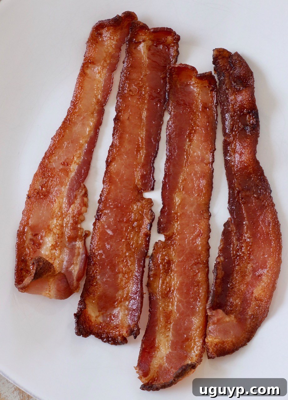 Perfectly cooked, crispy bacon strips arranged on a white plate, ready to be served for breakfast or as a versatile ingredient.