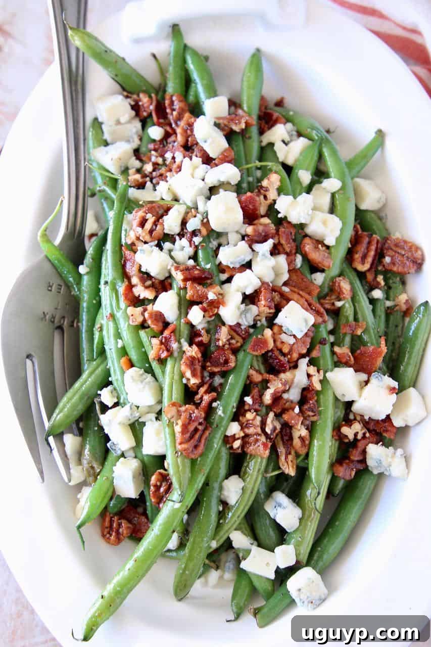 Fresh green beans in bowl topped with bacon crumbles, chopped pecans and blue cheese, a delicious side dish or salad component.