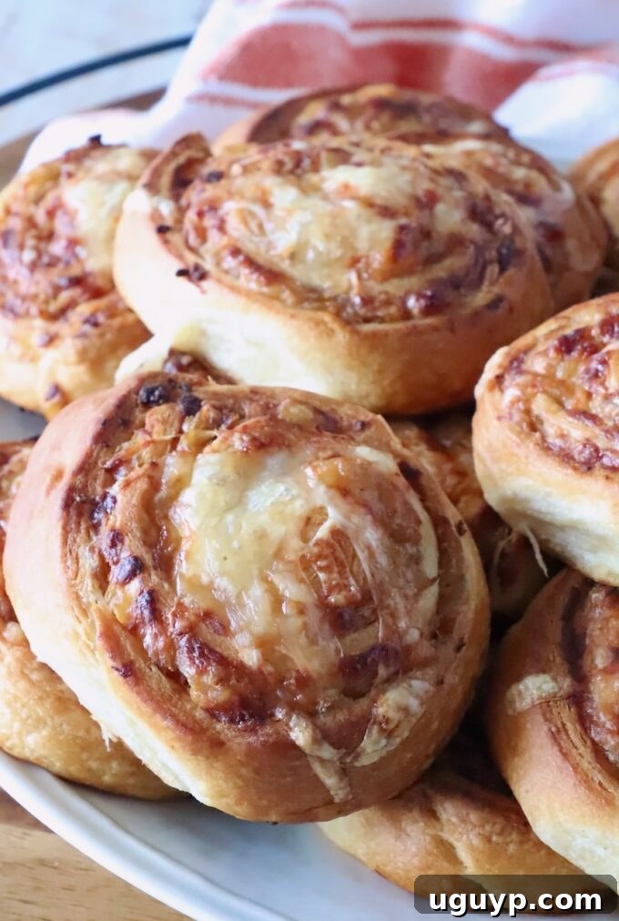 Close-up of golden-brown cheese and onion buns on a white plate. The swirled bread shows a crispy texture.