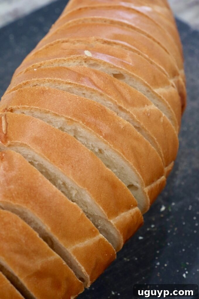 A French loaf of bread partially sliced on a cutting board.