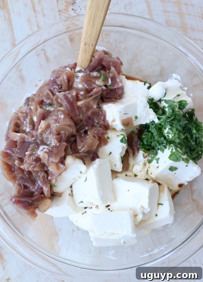 all ingredients for caramelized onion dip in a glass bowl, ready to be mixed with a spatula