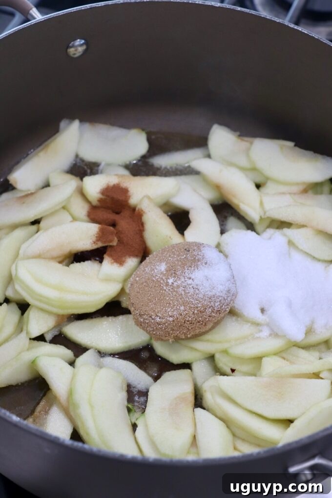 Apple slices simmering in a large skillet with sugar and cinnamon.