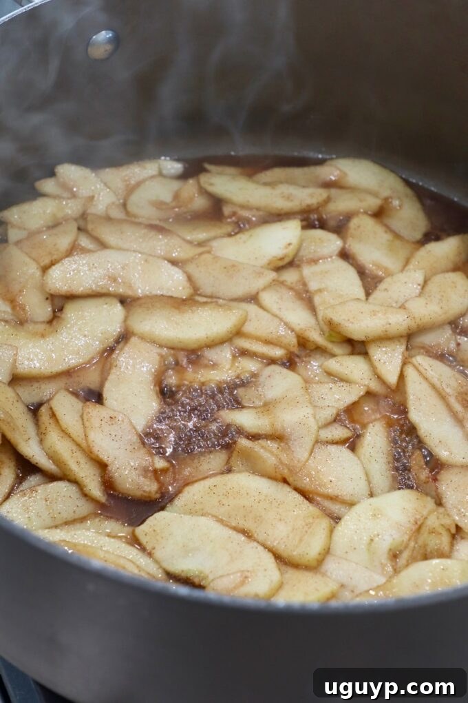 Cooked apple pie filling simmering in a skillet, appearing thickened and syrupy.