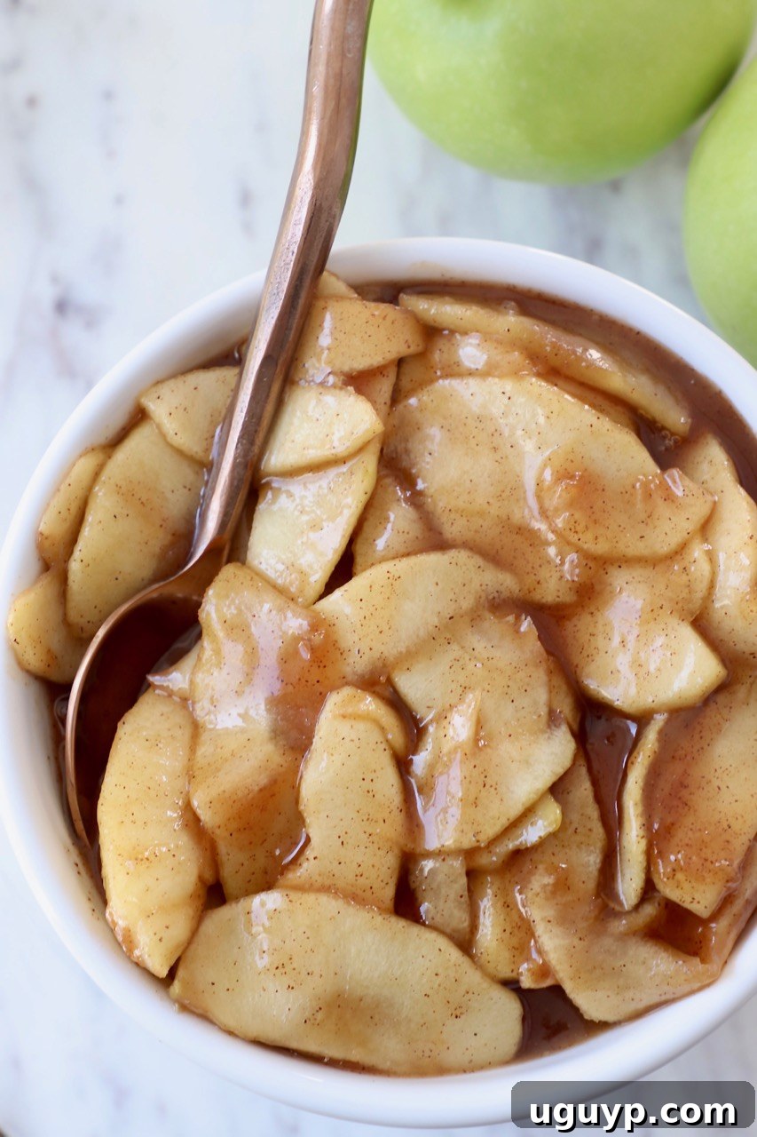 A beautiful bowl of prepared apple pie filling with a copper spoon resting in it, showcasing its perfect texture.