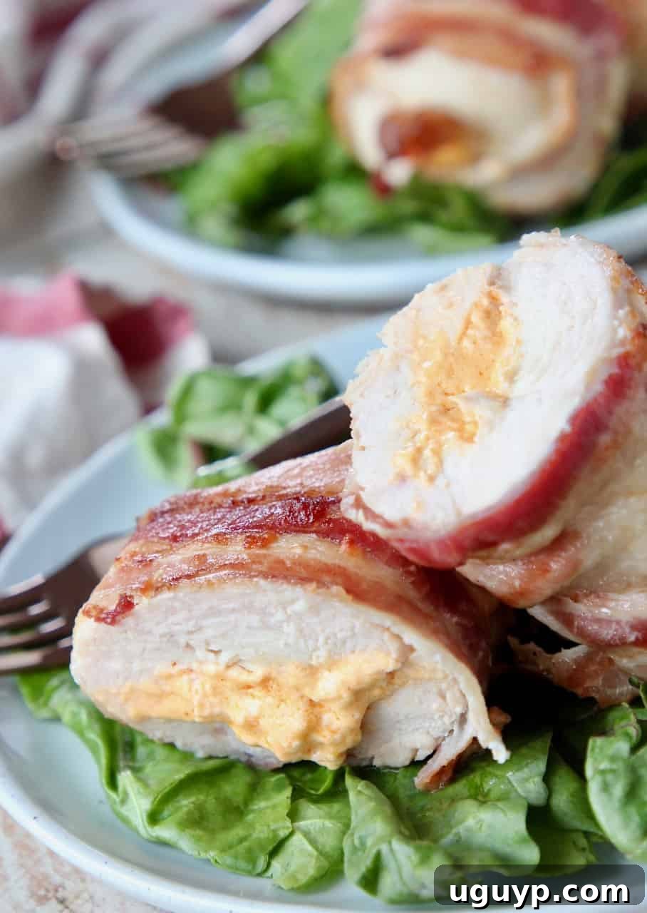 A perfectly sliced bacon wrapped cream cheese stuffed chicken breast on a plate, revealing its creamy filling, served alongside a fresh green salad.