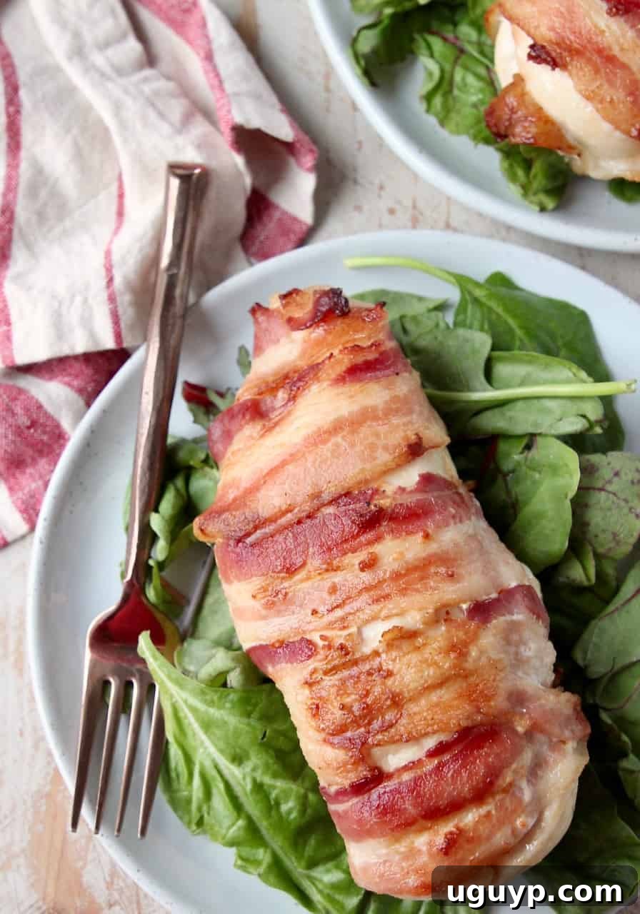 A perfectly cooked bacon wrapped stuffed chicken breast on a plate, ready to be enjoyed with a fork, accompanied by a light side salad.