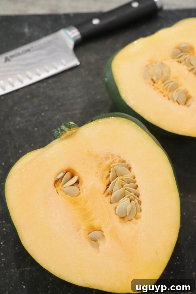 acorn squash sliced in half on cutting board, showing its vibrant orange flesh