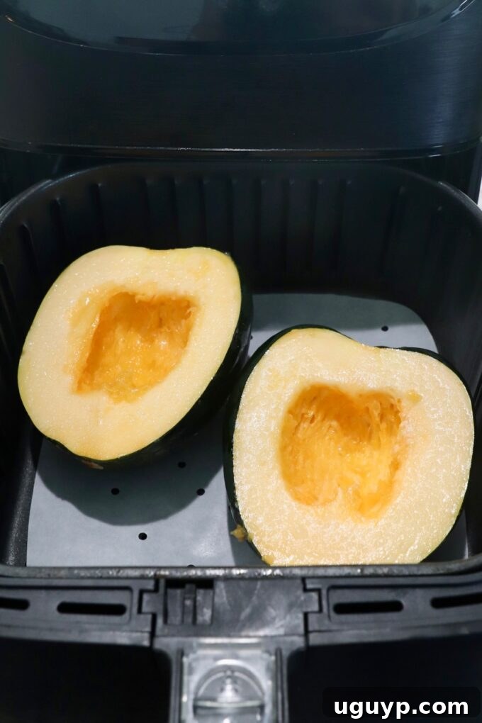 uncooked acorn squash cut in half and seasoned, placed in an air fryer basket