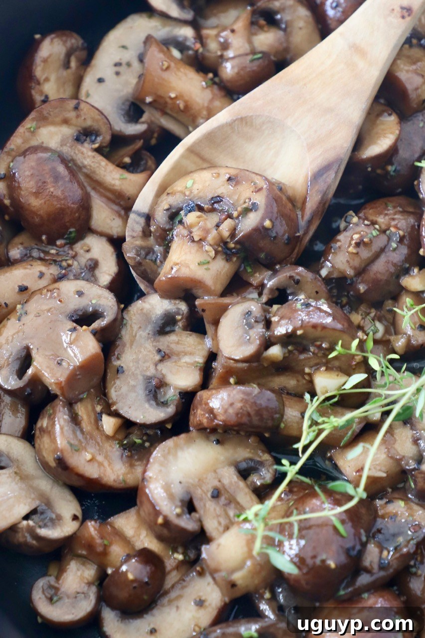 Cooked sliced mushrooms in a skillet with a wooden spoon, ready to be served