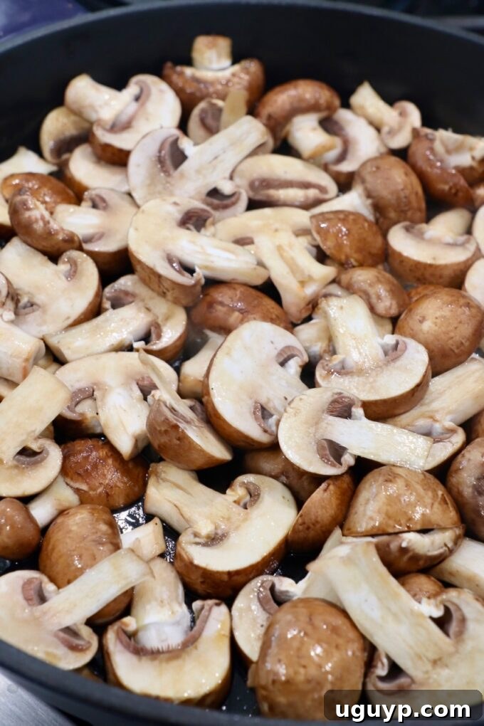 Sliced mushrooms being added to a hot skillet with melted butter and olive oil