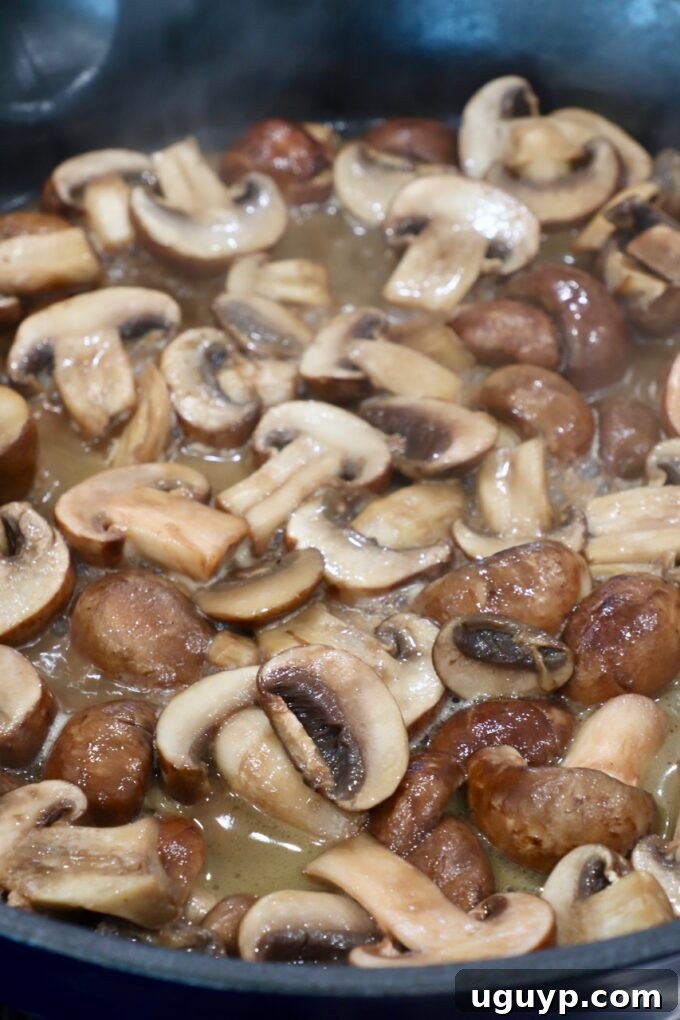 Sliced mushrooms cooking in broth in a skillet