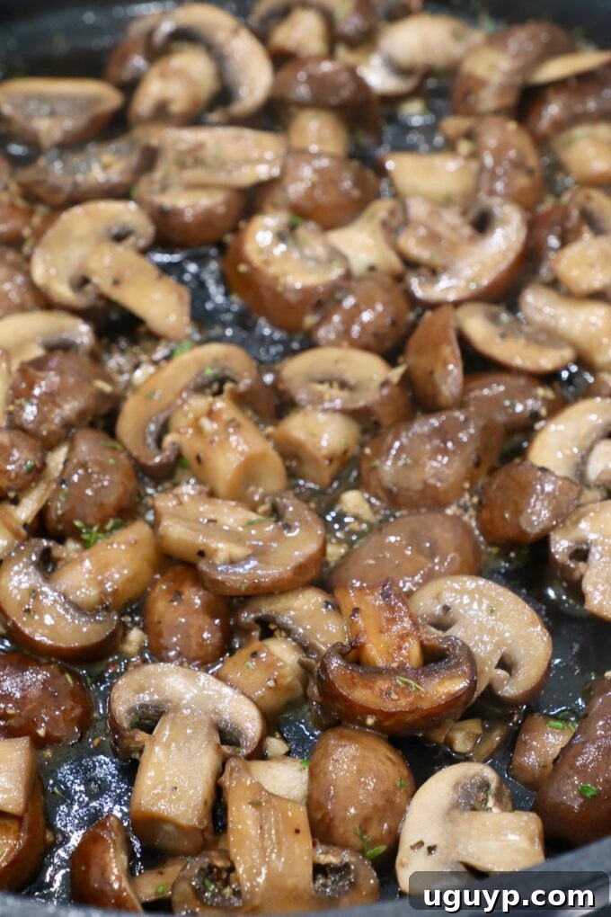 Cooked sliced mushrooms in a skillet with garlic and thyme added