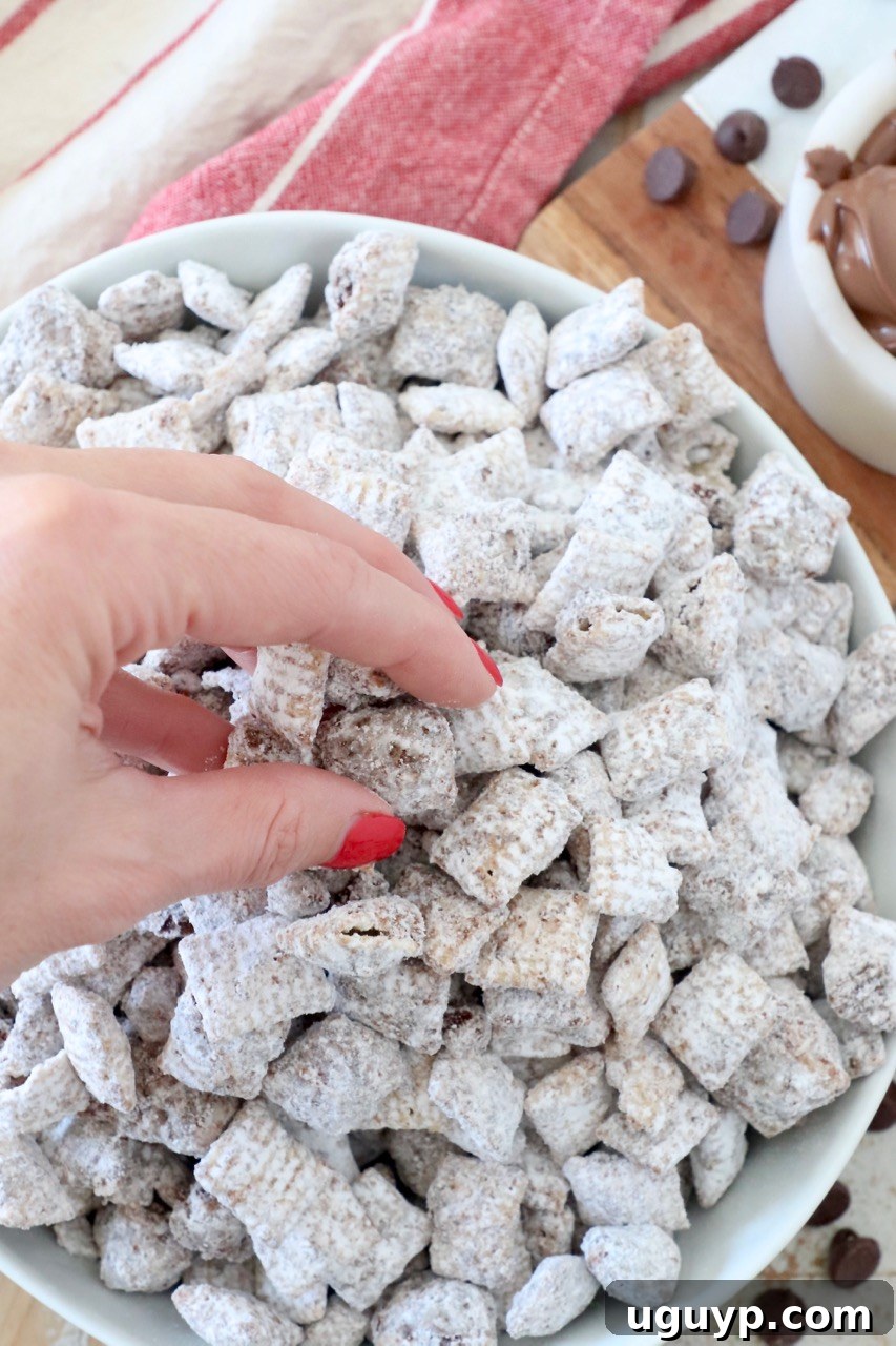 A hand reaching into a white bowl to grab a handful of Nutella Muddy Buddies.