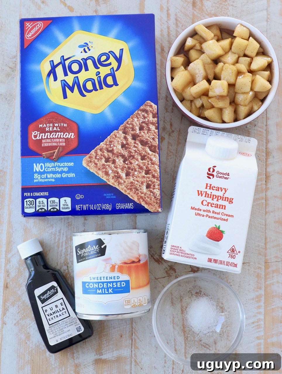 Key ingredients for making homemade apple pie ice cream laid out, including a can of condensed milk, heavy cream, fresh apples, vanilla extract, and graham crackers.