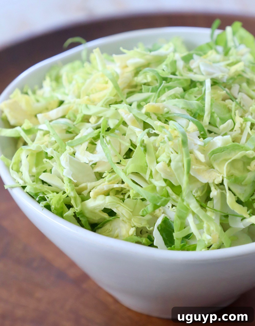 A large, rustic white bowl abundantly filled with freshly shredded Brussels sprouts, signifying a successful preparation and readiness for cooking.