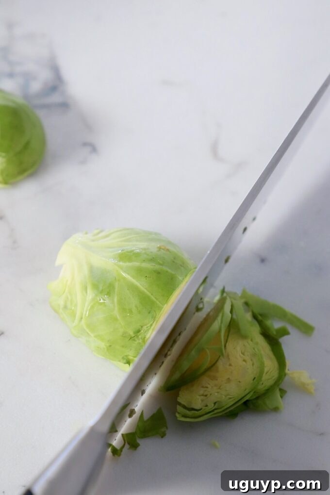 Thinly sliced Brussels sprouts pile up on a cutting board as a knife expertly shreds them into fine ribbons.