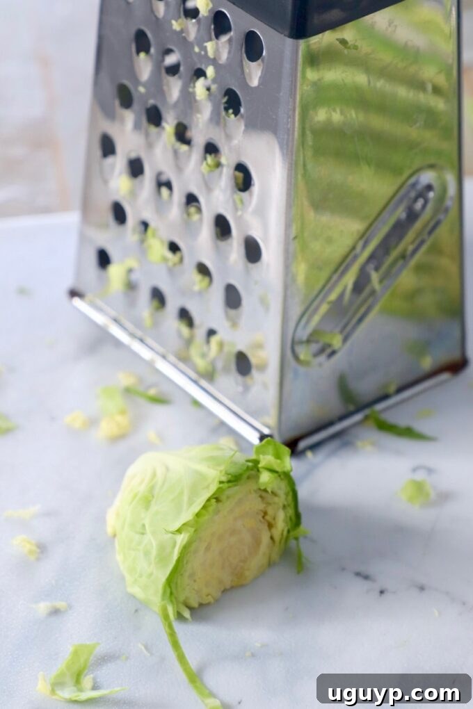 A half-cut Brussels sprout positioned next to a box grater on a cutting board, illustrating a less effective shredding method.