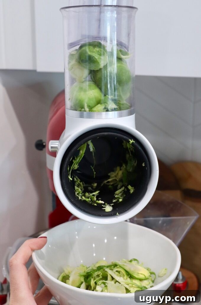 Brussels sprouts loaded into the grater attachment of a KitchenAid stand mixer, ready for high-speed shredding.