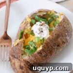 baked potato on plate with fork, filled with cheese, green onions and sour cream