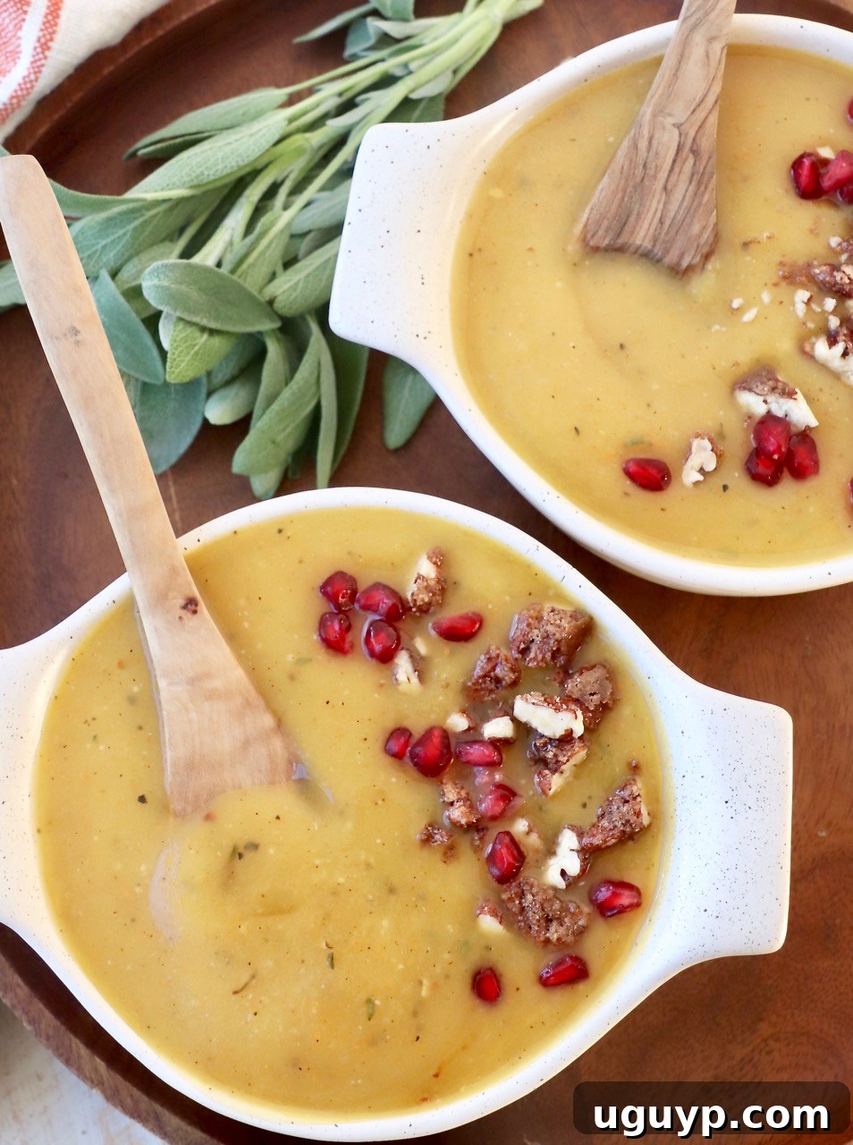 acorn squash soup in two bowls with spoons topped with walnuts and pomegranate seeds