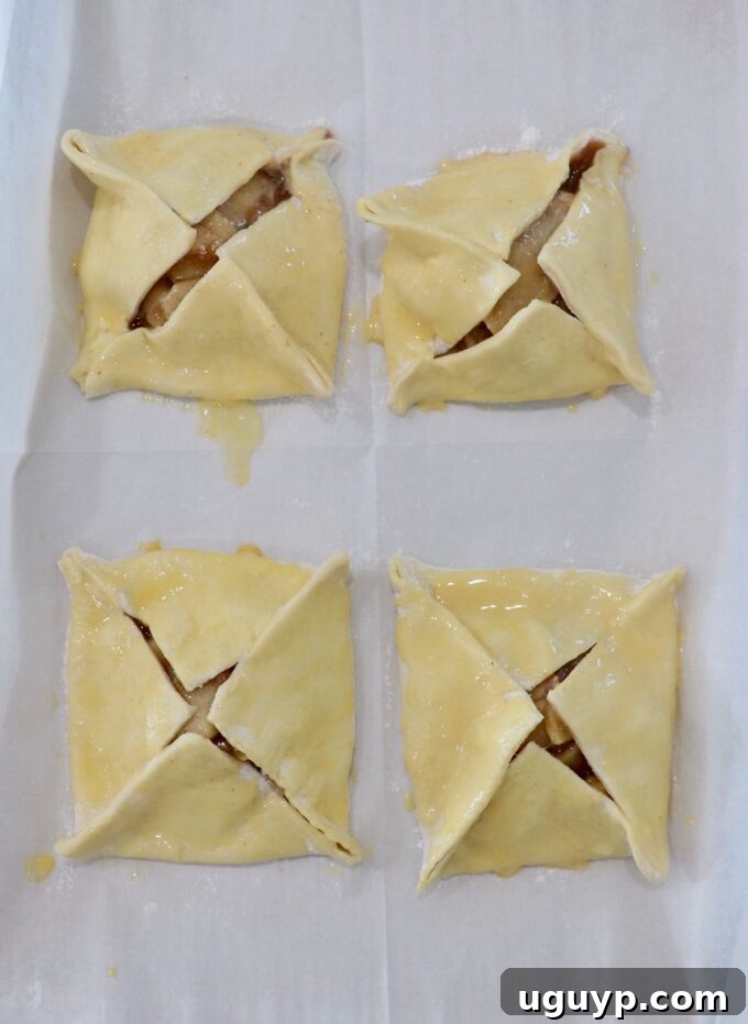 four uncooked apple danish brushed with egg wash on parchment paper
