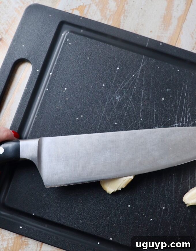 Chef's knife smashing a garlic clove on a cutting board