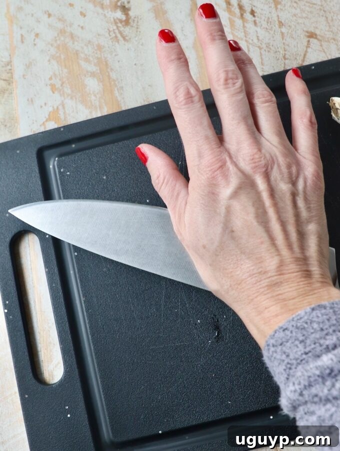 Hand pressing a chef's knife onto a garlic clove on a black cutting board
