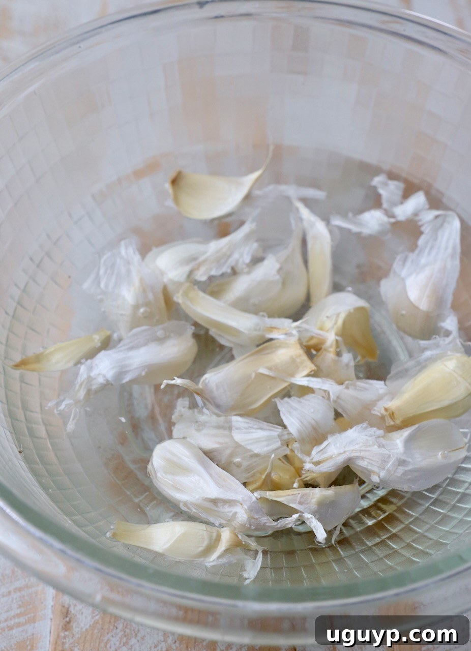 Unpeeled garlic cloves submerged in a glass bowl of water