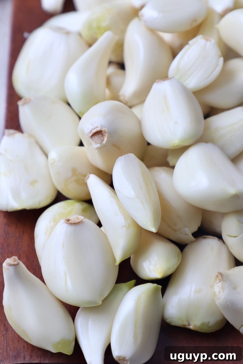 Perfectly peeled cloves of garlic resting on a brown cutting board