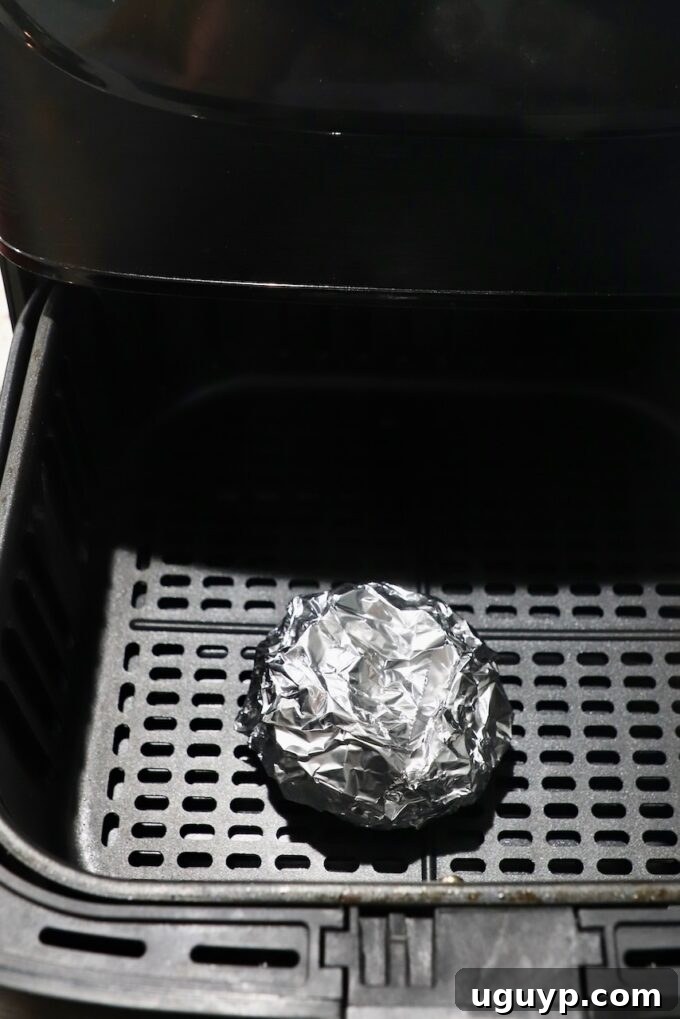 Garlic head wrapped in foil, placed inside an air fryer basket.