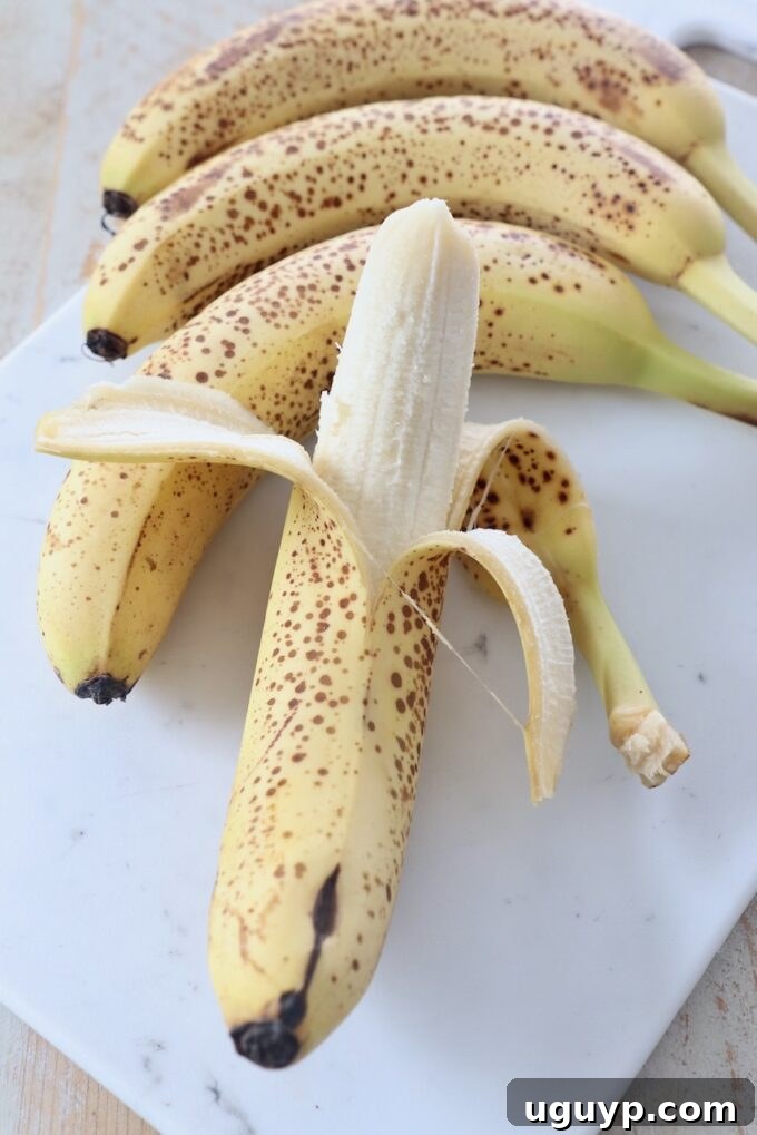 Whole bananas on cutting board with one partially peeled, illustrating ripeness.