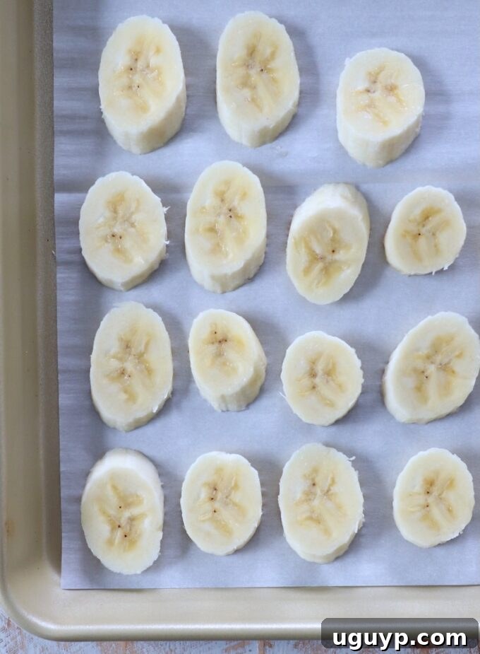 Banana slices arranged on a parchment-lined baking sheet for flash freezing.