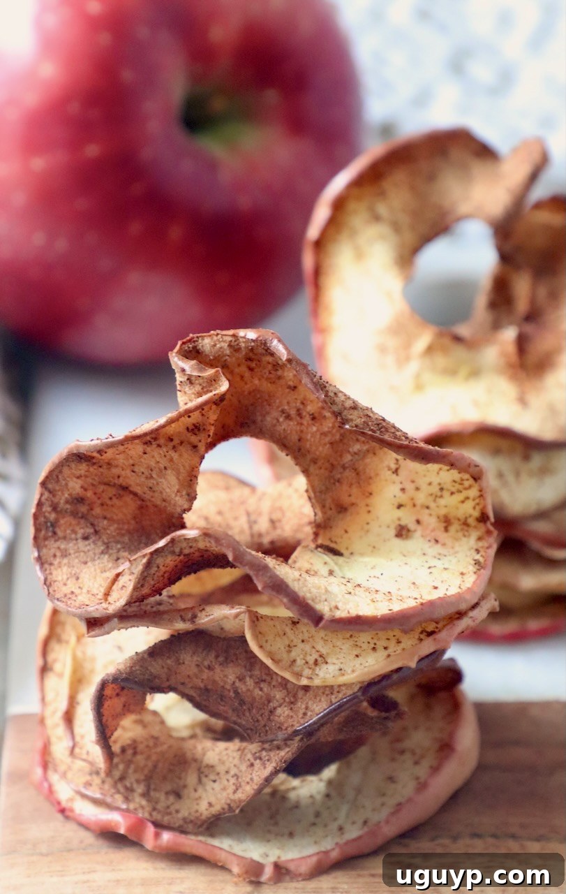 Stacked homemade apple chips on a wooden cutting board next to a fresh whole apple