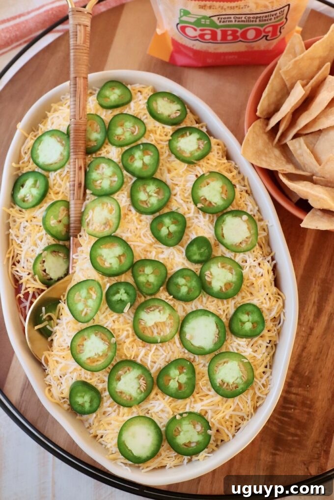 Finished seven layer dip in a casserole dish with a serving spoon, garnished with jalapenos