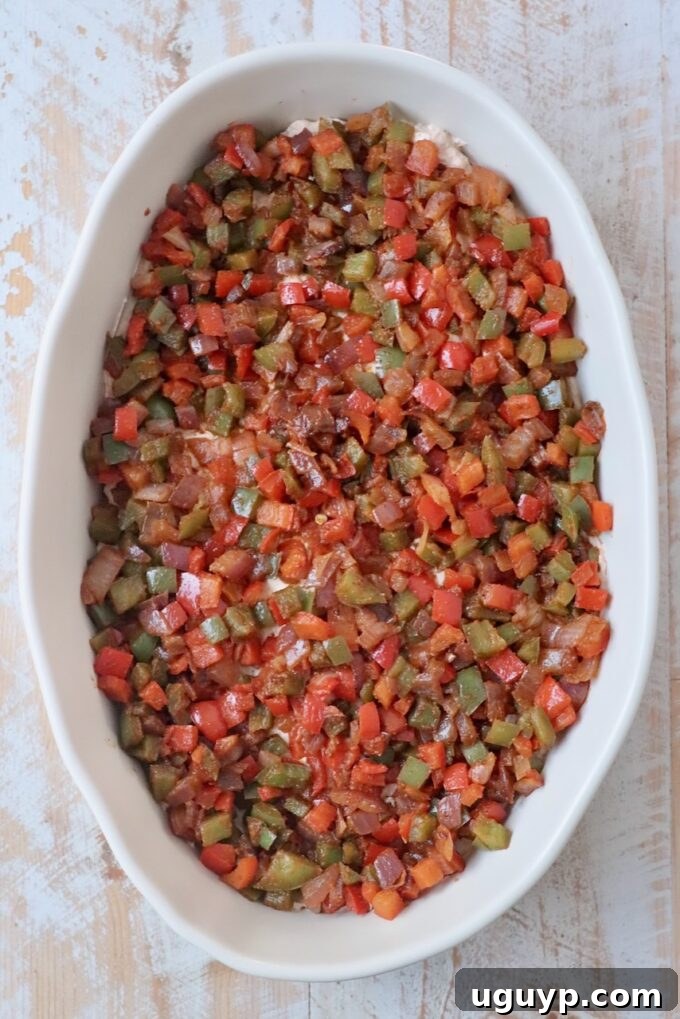 Sautéed diced fajita vegetables layered in a casserole dish, over the cream cheese