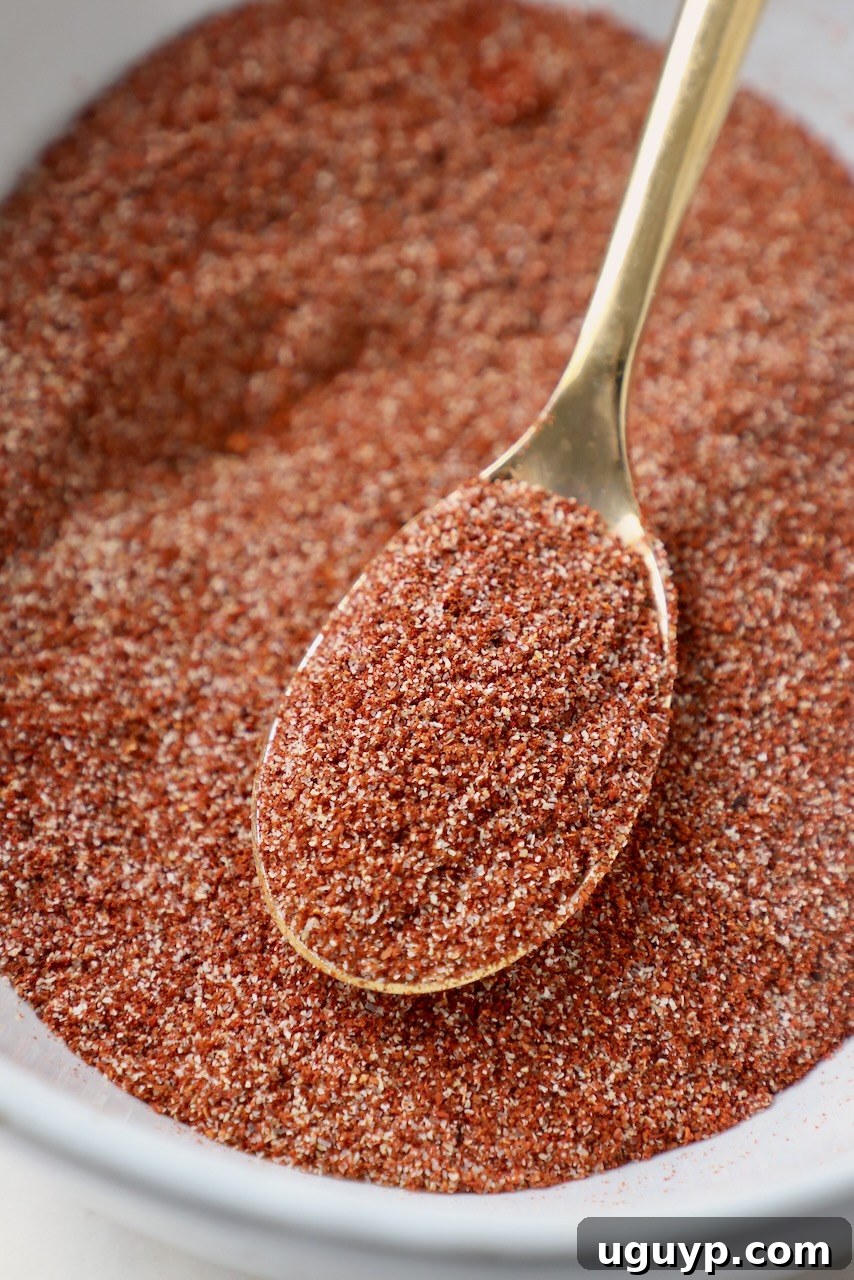 A bowl of freshly mixed chicken wing dry rub with a gold spoon resting inside, showcasing its vibrant color and texture.