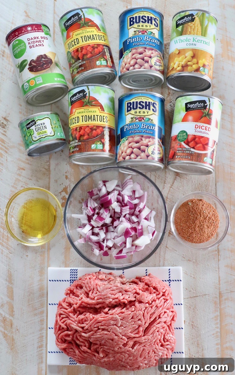 A rustic wooden board showcasing all the fresh and canned ingredients needed for making Slow Cooker Taco Soup, including ground beef, onions, various canned goods, and spices.