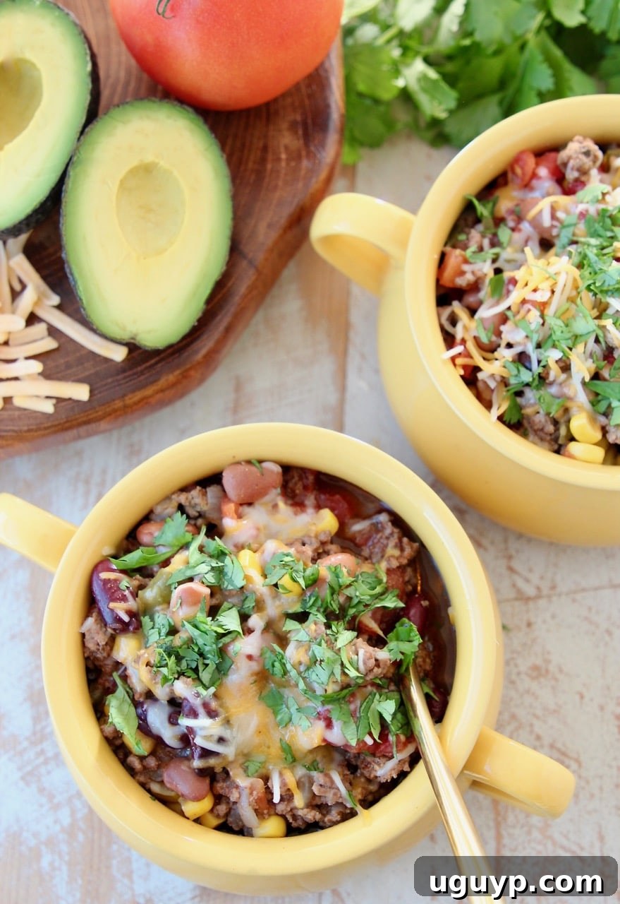 Multiple yellow crocks filled with Slow Cooker Taco Soup, topped with fresh avocado, cilantro, and shredded cheddar cheese, with a gold spoon in one bowl.