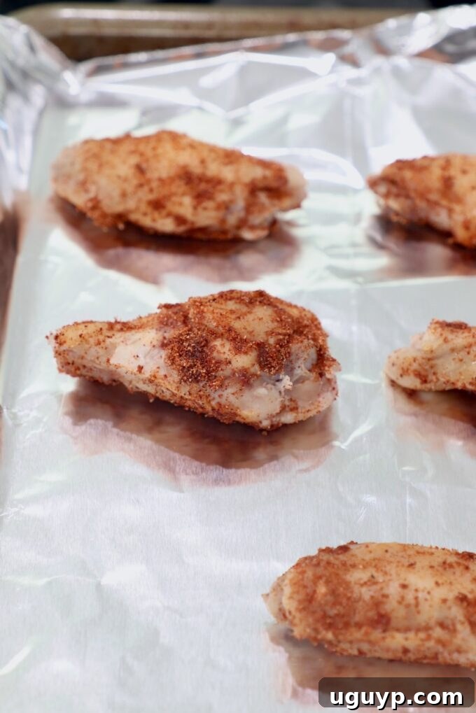 Seasoned chicken wings arranged in a single layer on a foil-lined baking sheet, prepared for oven broiling.