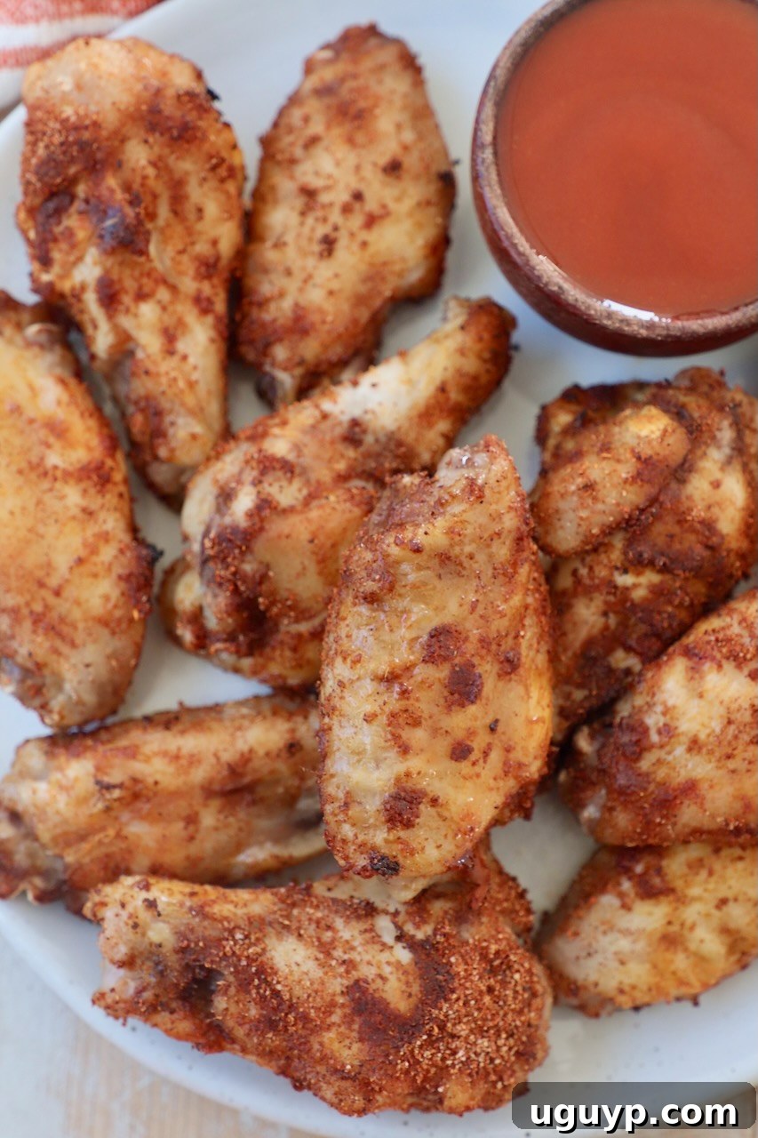 Crispy, sauced sous vide chicken wings artfully arranged on a plate, with a small bowl of buffalo sauce on the side for dipping.