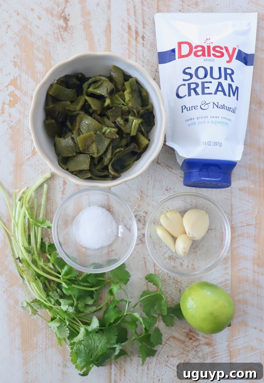 Fresh ingredients for poblano sauce, including whole poblano peppers, garlic, lime, and cilantro, artfully arranged on a white wood cutting board.