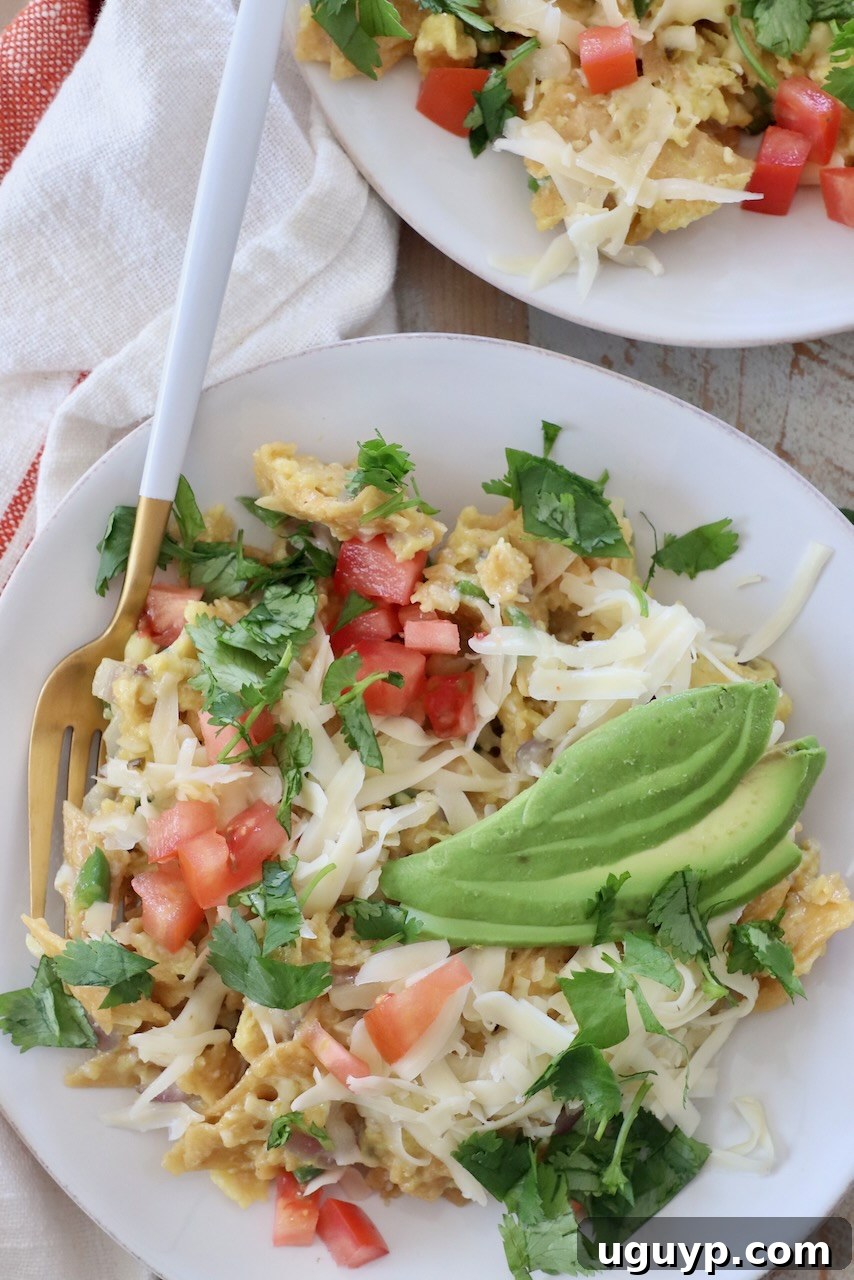 migas on a white plate topped with sliced avocado