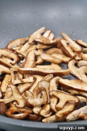 Sliced shiitake mushrooms cooking in a wok with soy sauce.