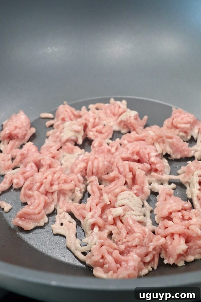 Ground pork sizzling and browning in a large wok over medium-high heat.